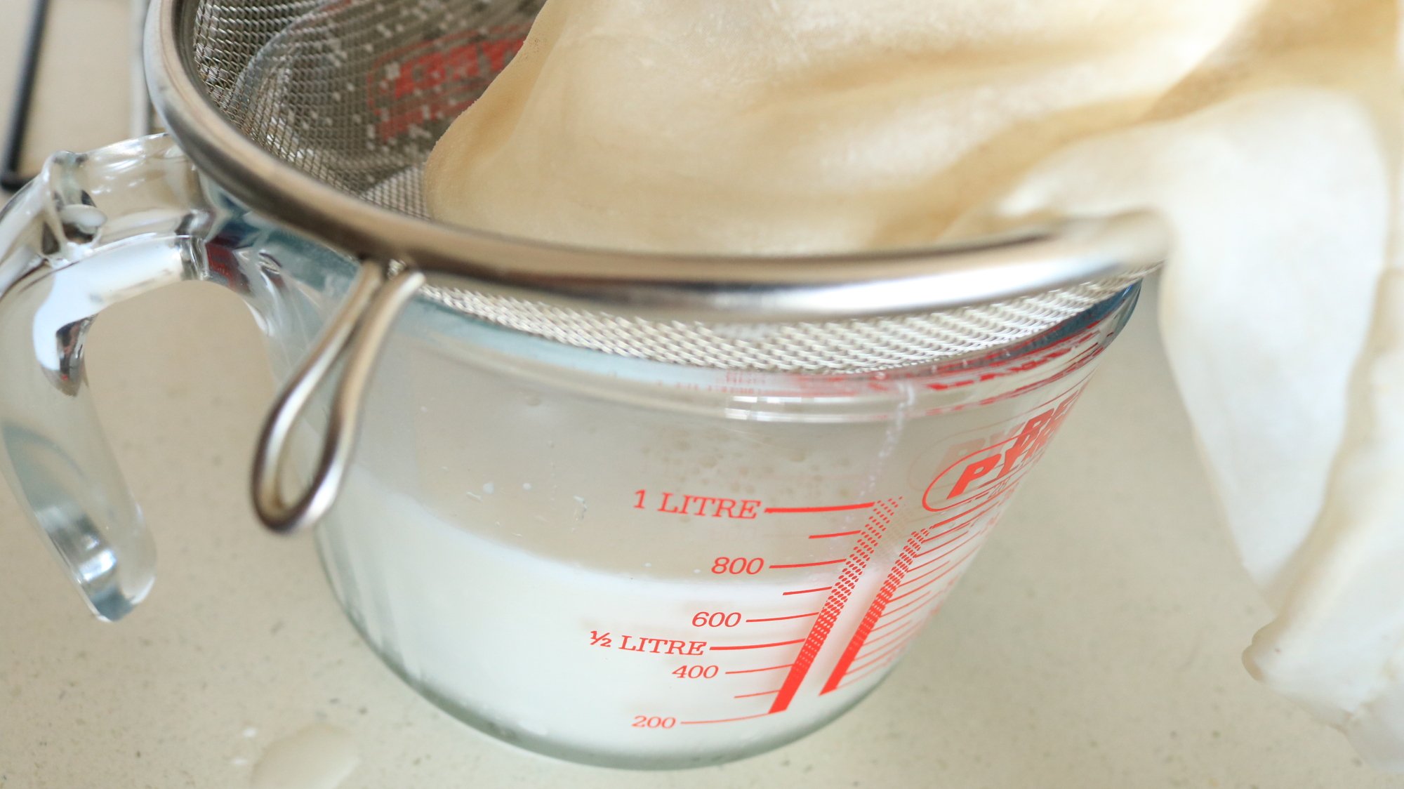 A nut milk bag in a strainer over a measuring cup.